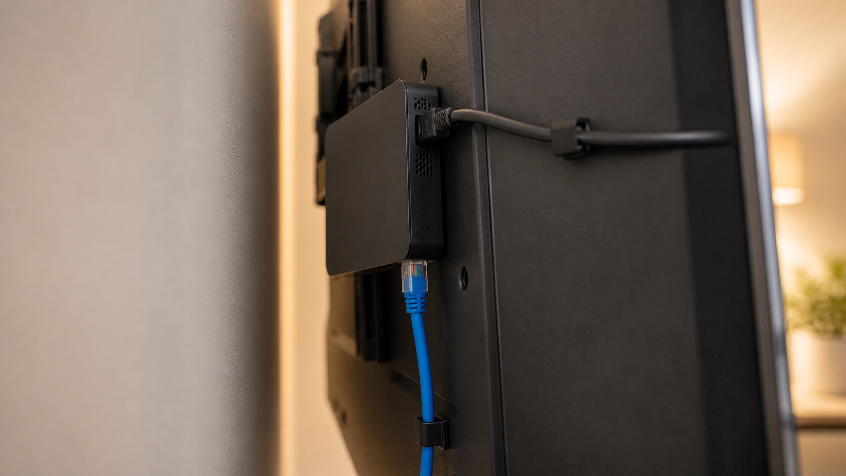 Player compacto preso atrás de uma televisão, ligado por cabo HDMI e cabo de rede
